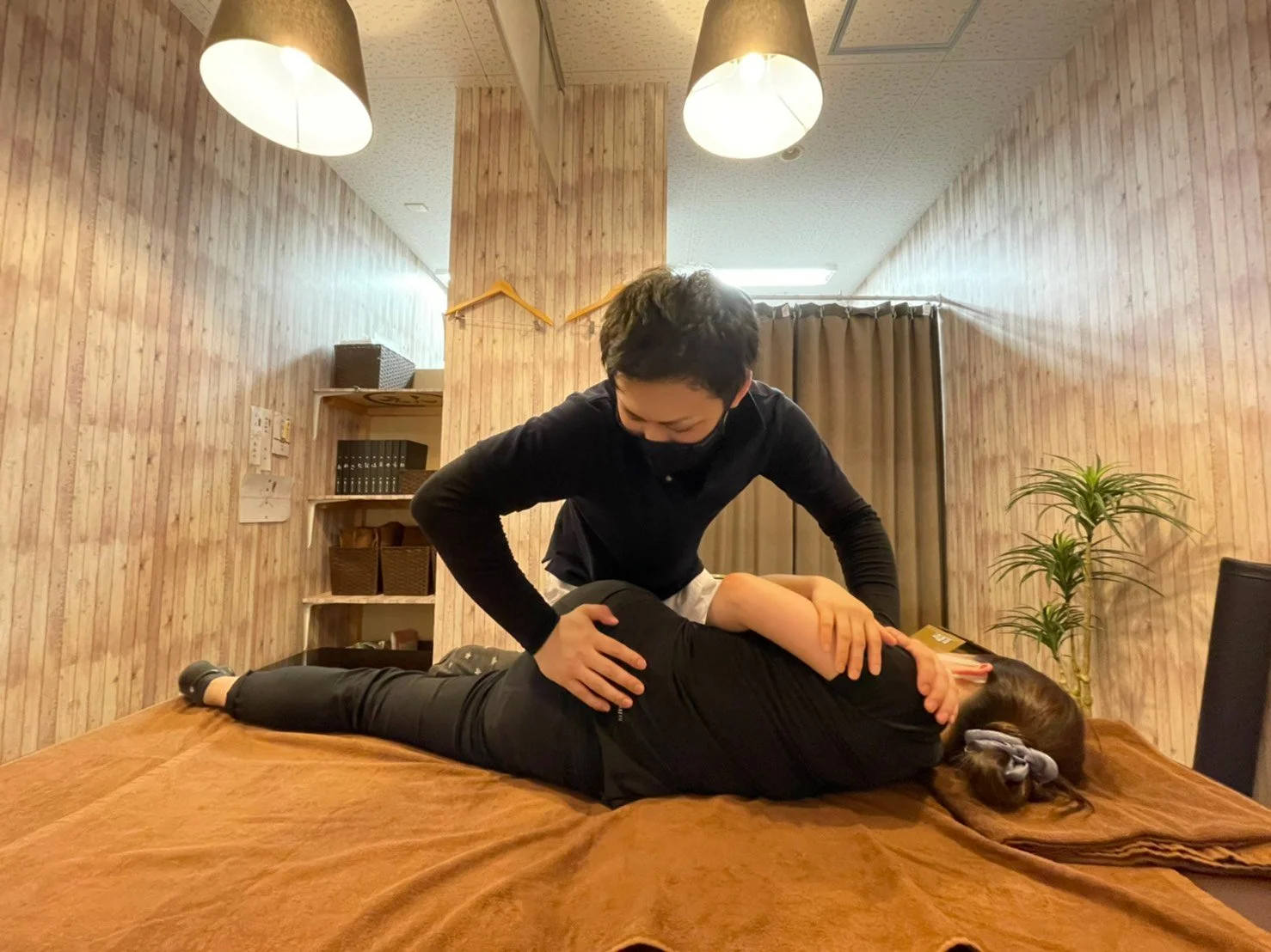 木目調の壁に囲まれた施術室で、スタッフがお客様に施術をしている様子